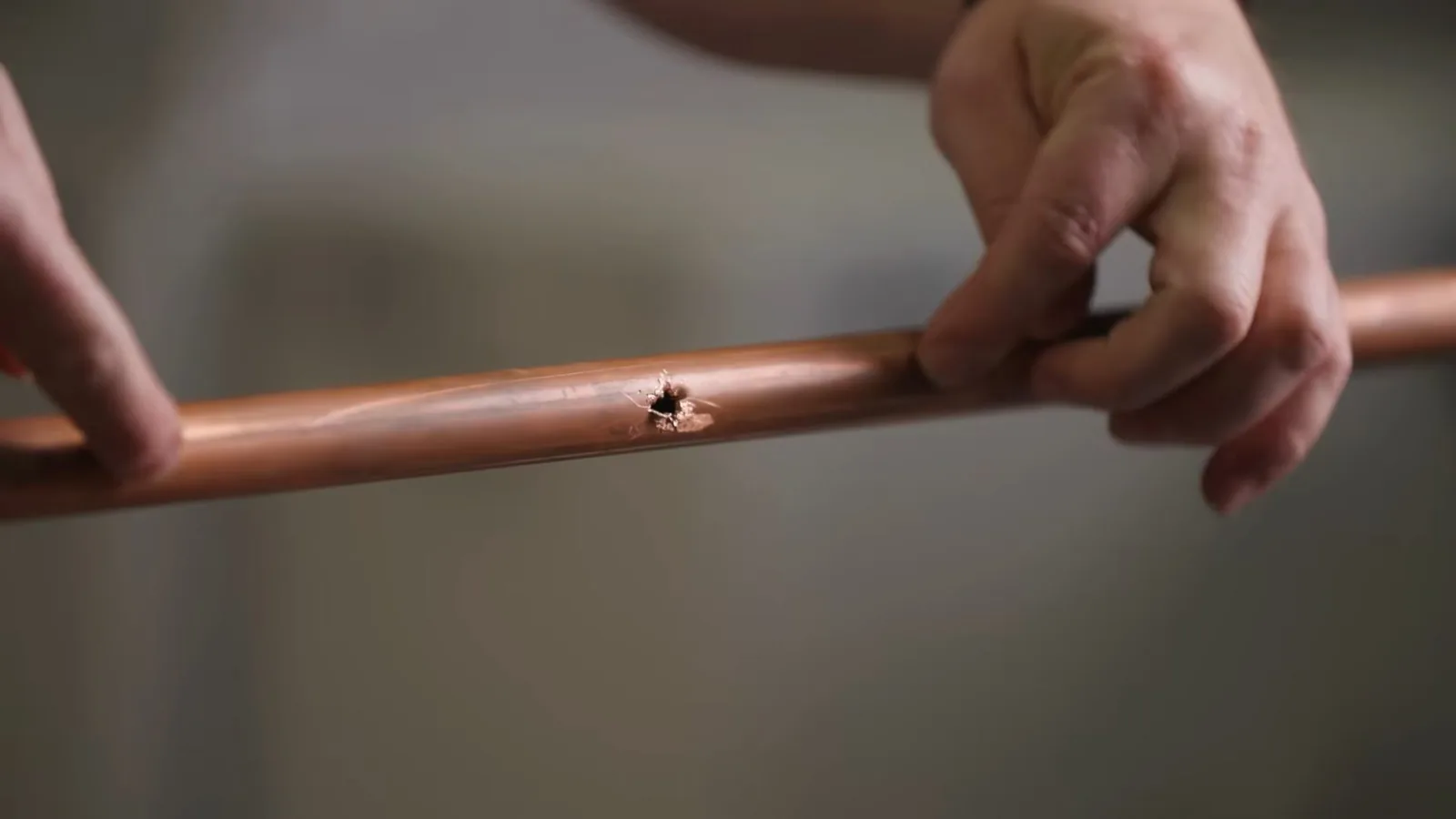 Two hands holding a length of copper pipe that has a small hole in its side.