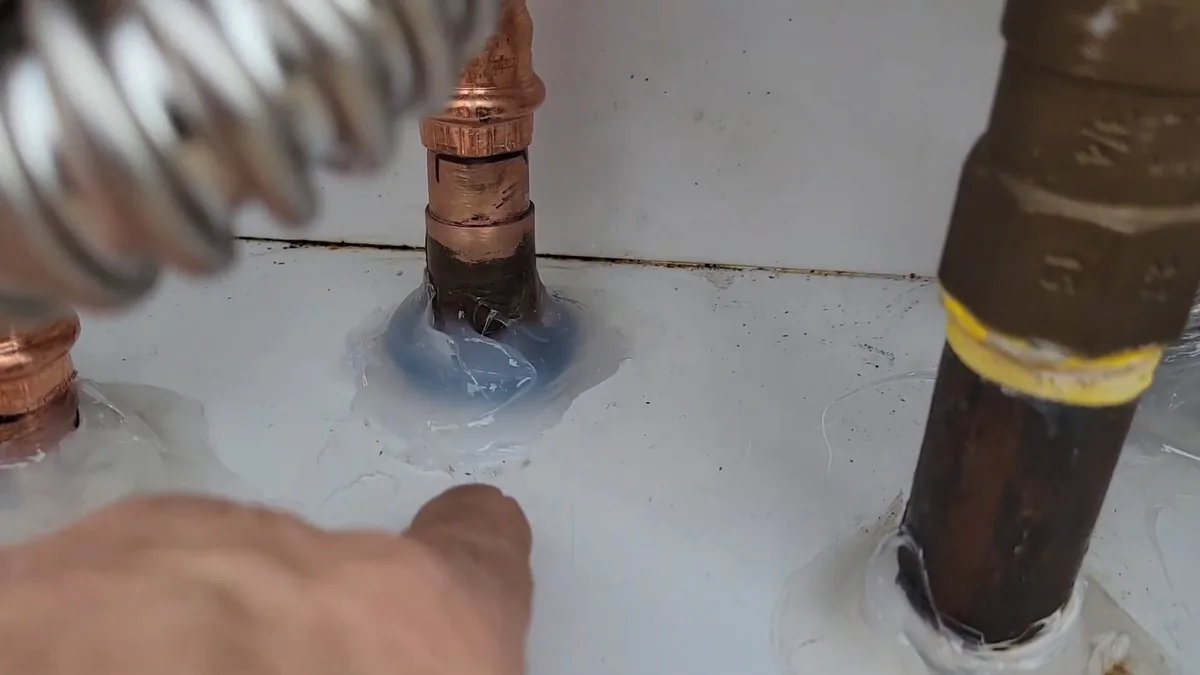 Corrugated gas line, a copper fitting and a brass nipple connected at the top of a heater, with a finger beside the sealed joint.