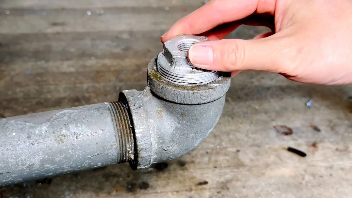 Hand turning the threaded cap on a galvanized cleanout fitting at the end of a pipe.