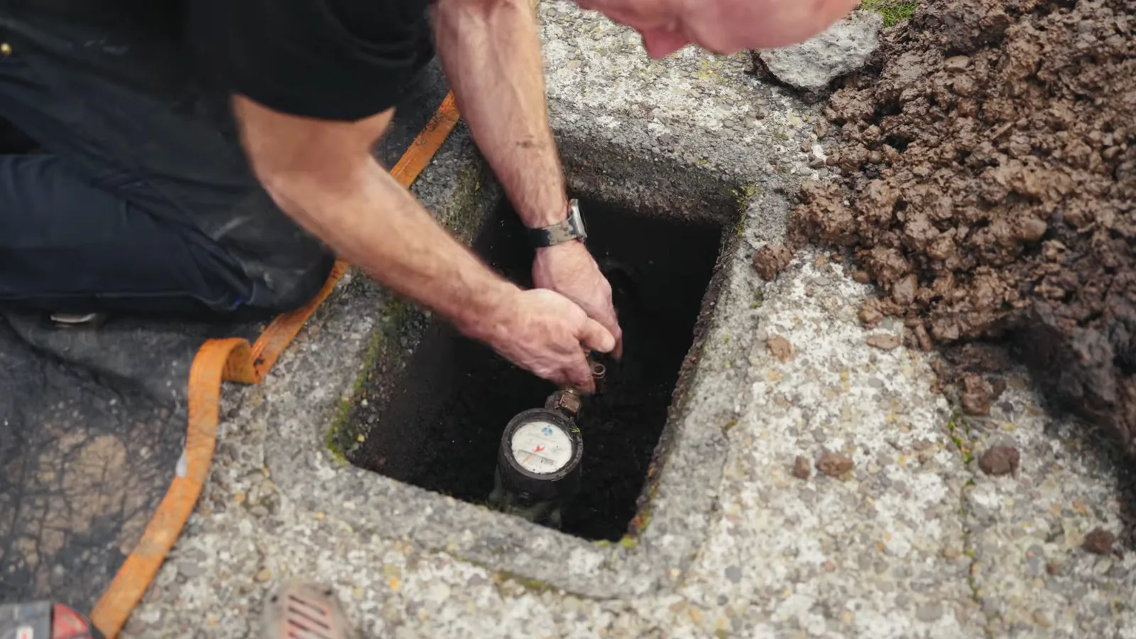Man kneeling beside a concrete ground box and reaching in toward a water meter.