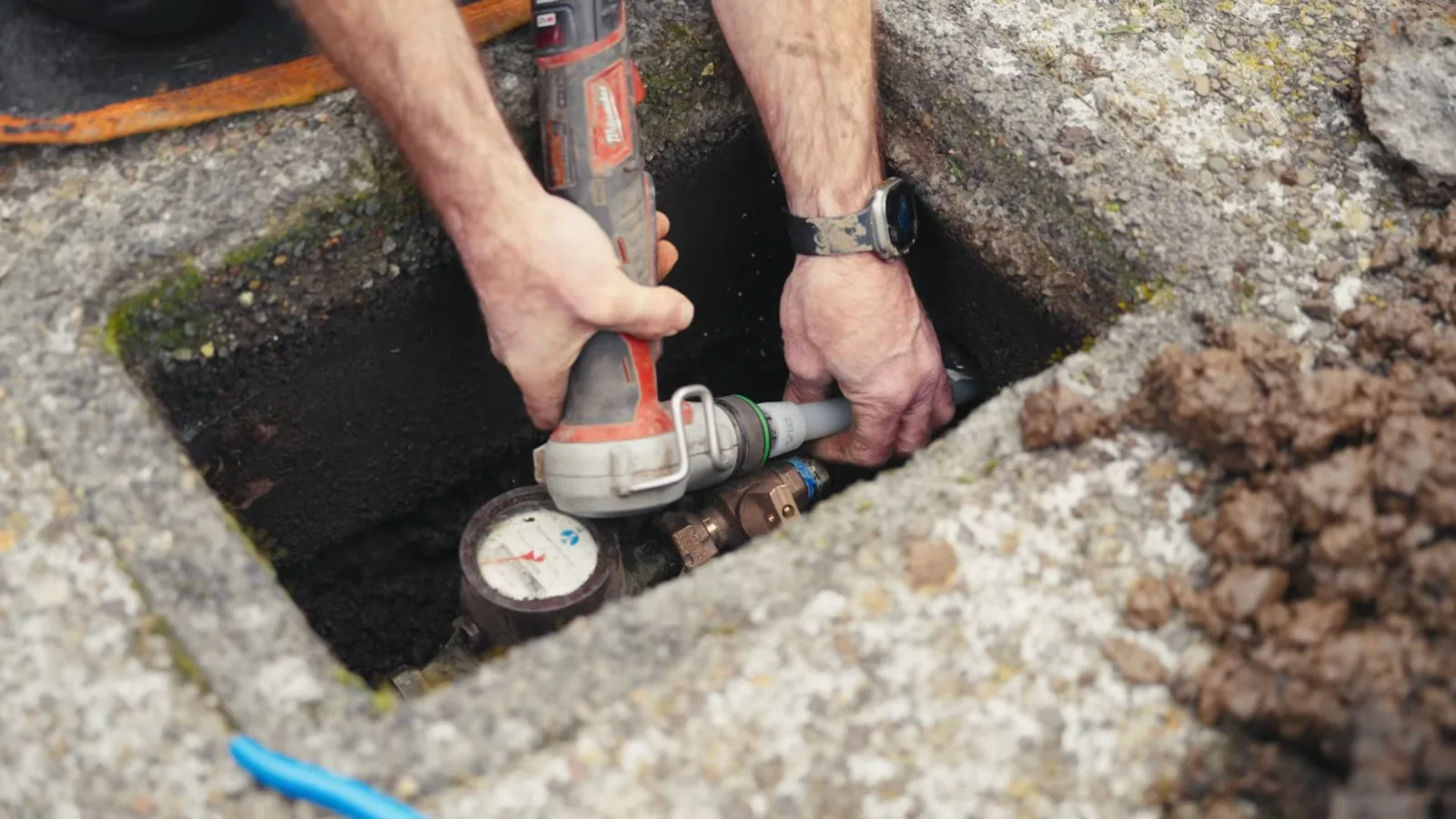 Man holding a power tool at a water meter inside a concrete ground box.