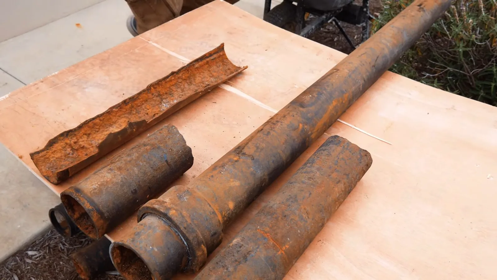Several rusted lengths of cast iron pipe on a plywood sheet, one split open lengthwise.