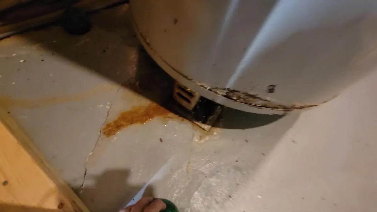 Rust-colored staining on the floor at the base of a white water heater, with rust on the tank's bottom rim.