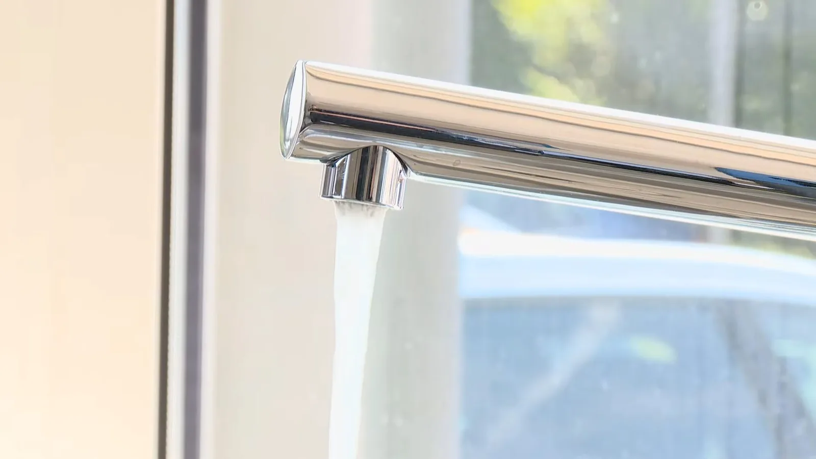 Water running from a polished chrome faucet beside a bright window.